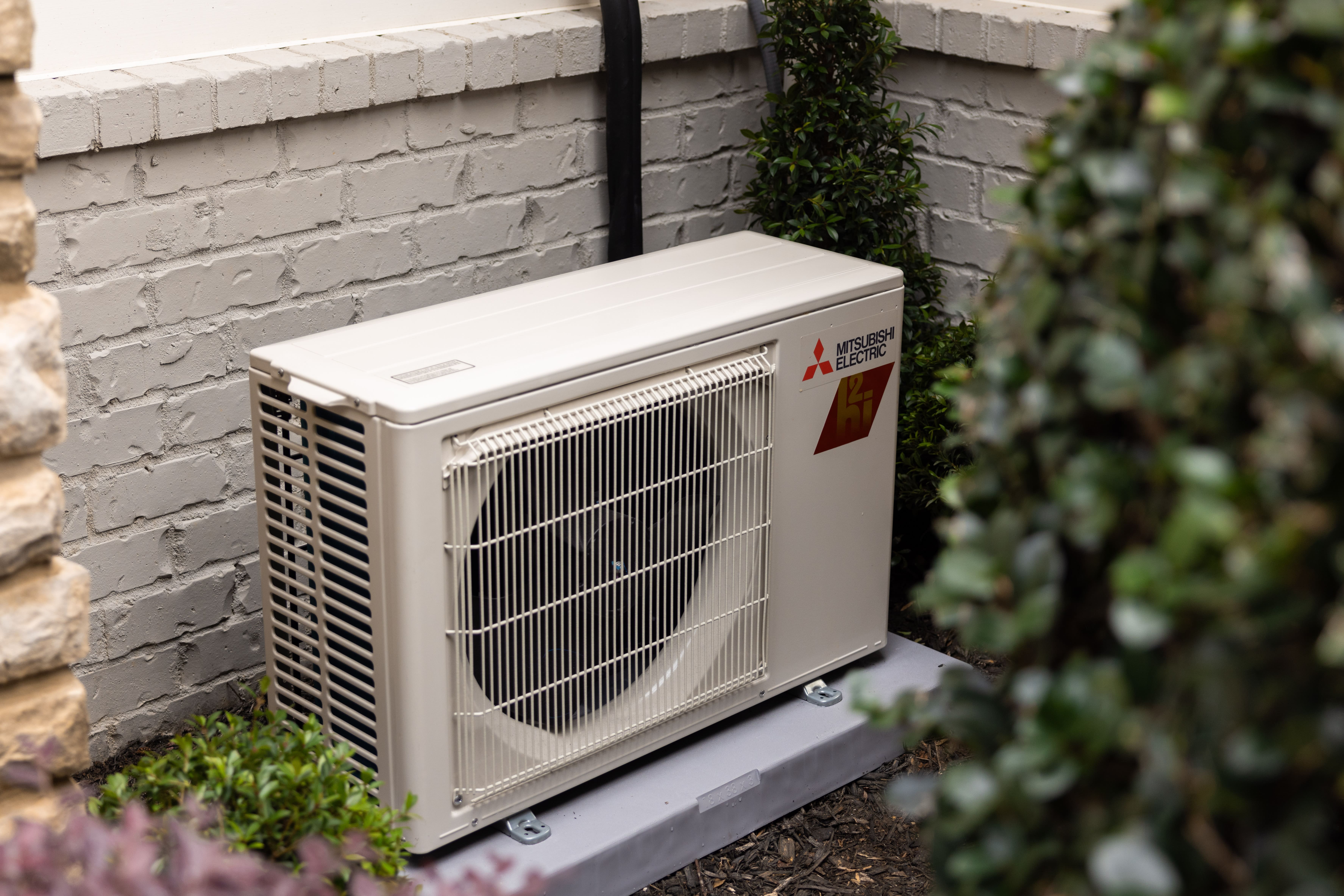 Mitsubishi Electric outdoor air conditioning unit installed beside landscaped greenery.
