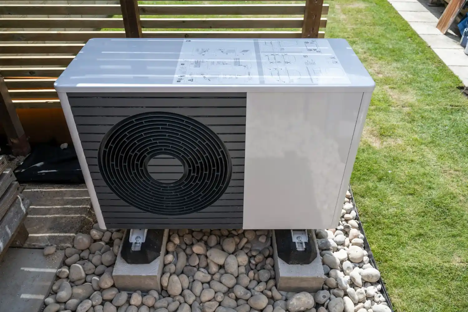 A white and grey Viessmann Vitocal 262-A heat pump unit sits on concrete blocks surrounded by pebbles in a residential outdoor setting with grass and a wooden fence.