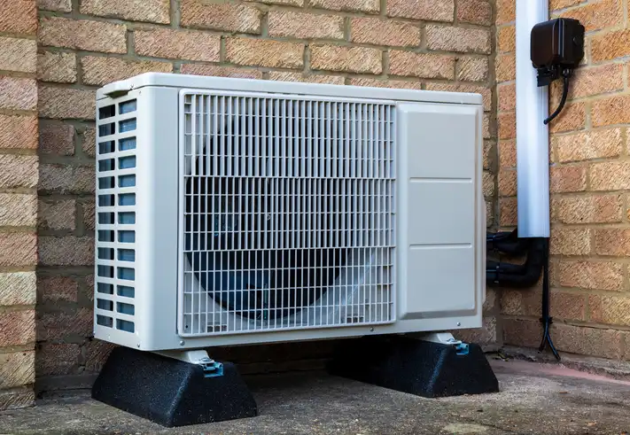 An outdoor heat pump unit is installed against a brick wall.