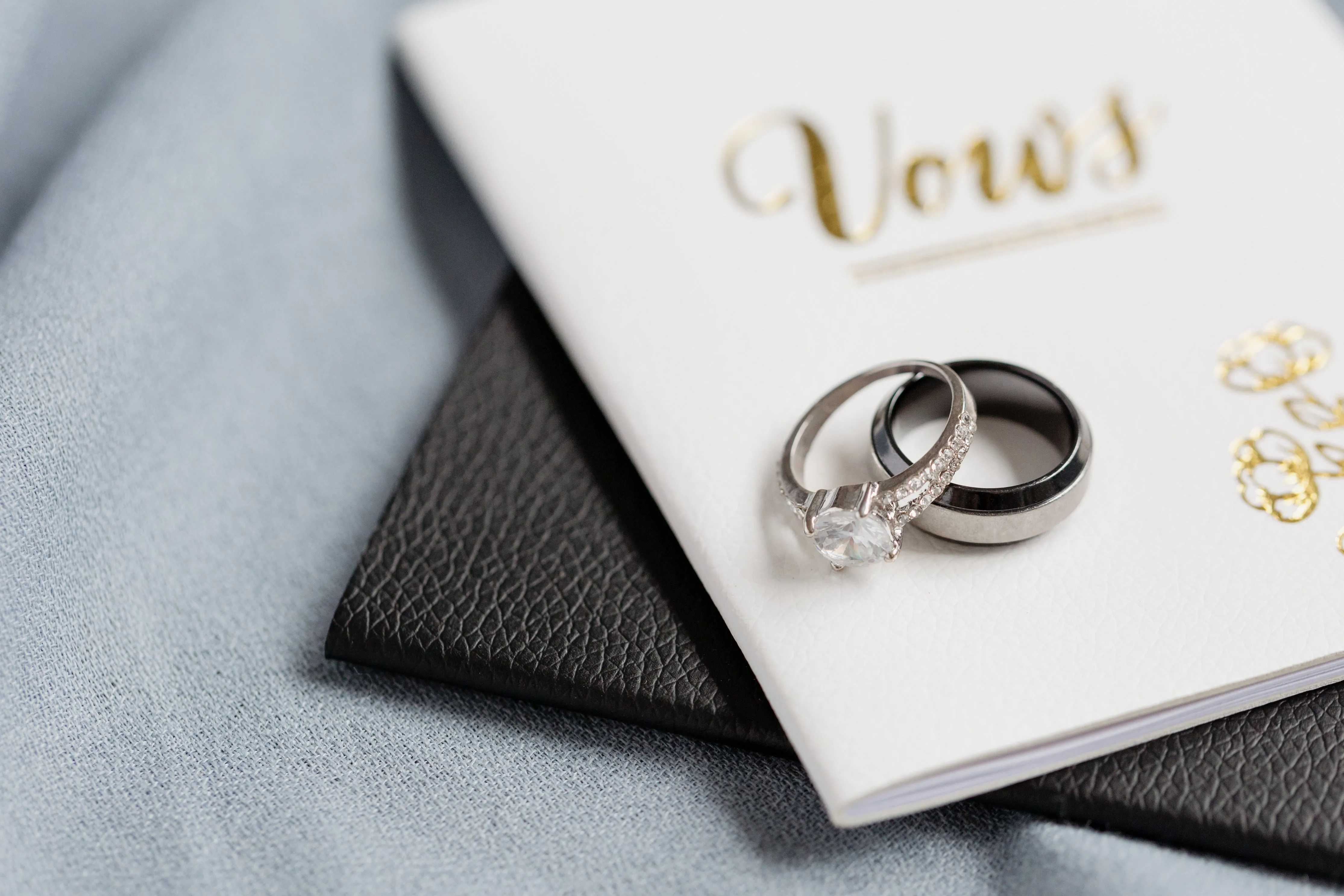 Two wedding rings on a white vow book with gold lettering.