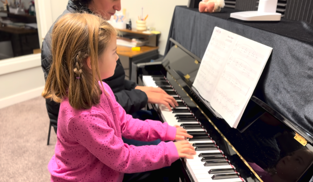 Piano teacher with kid student playing piano together