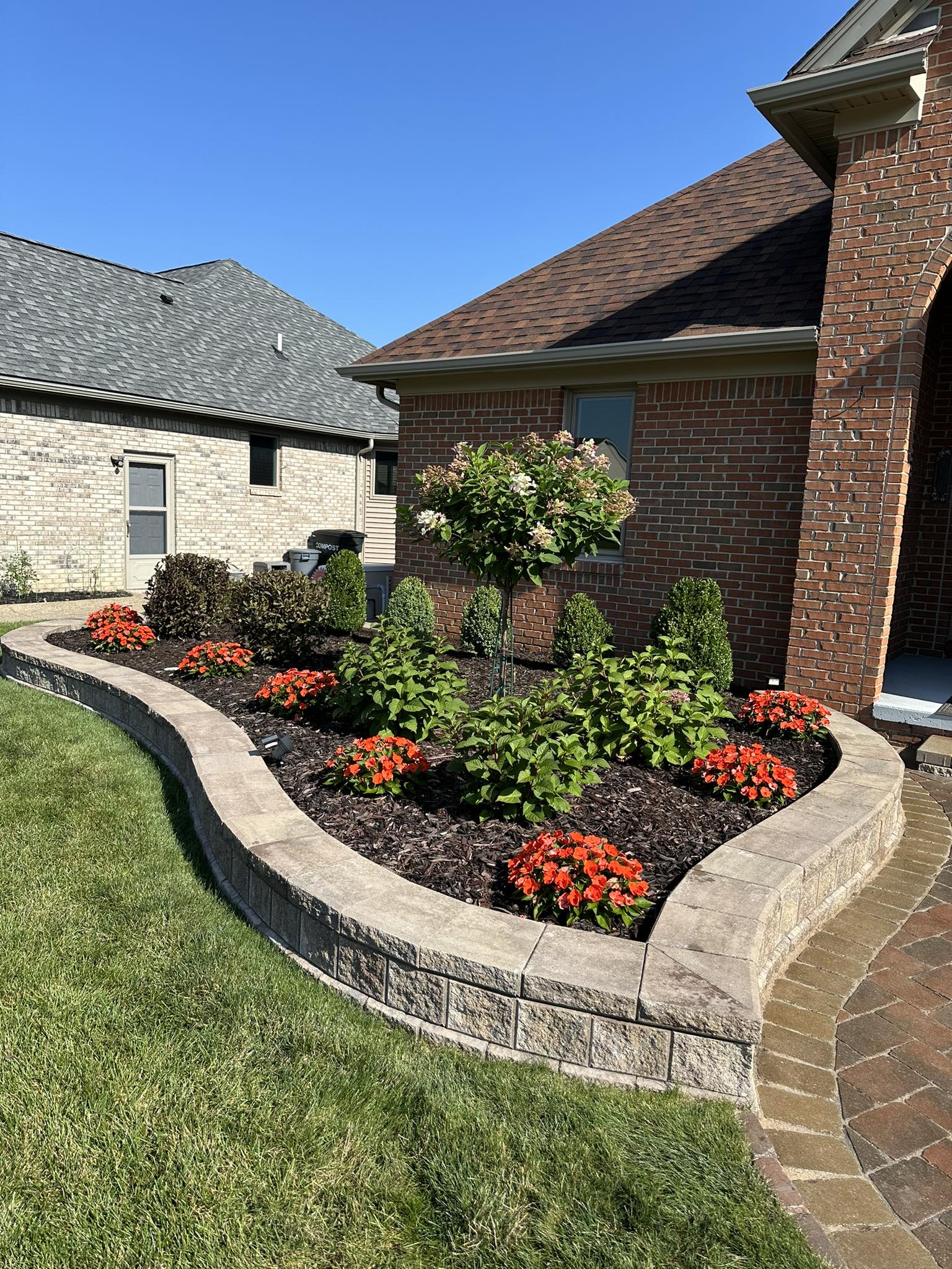 Curved stone retaining wall with vibrant flower bed installation and manicured shrubs by JB Landscaping in Macomb, MI
