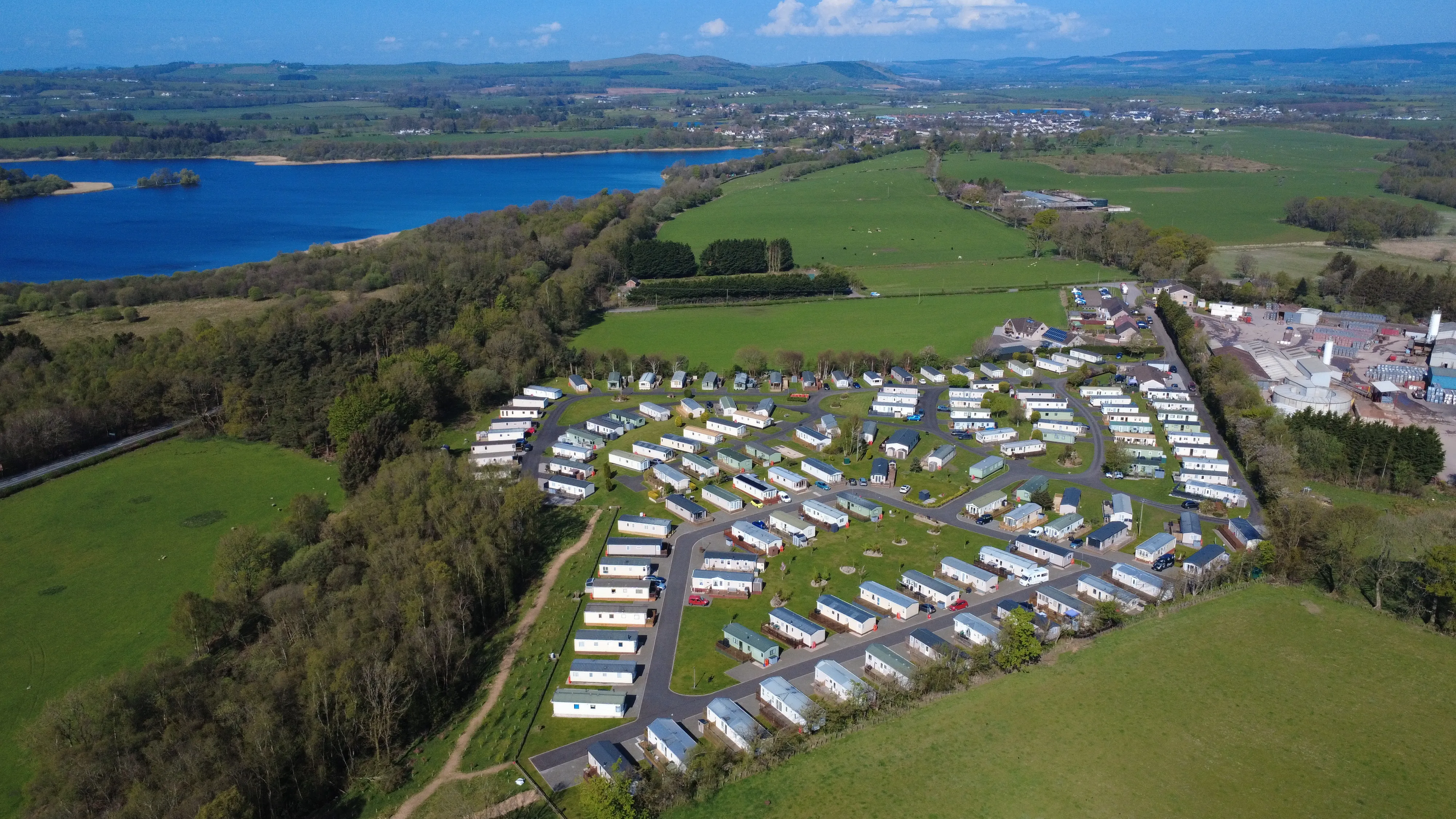 Aerial view of mobile home park near blue lake and green countryside
