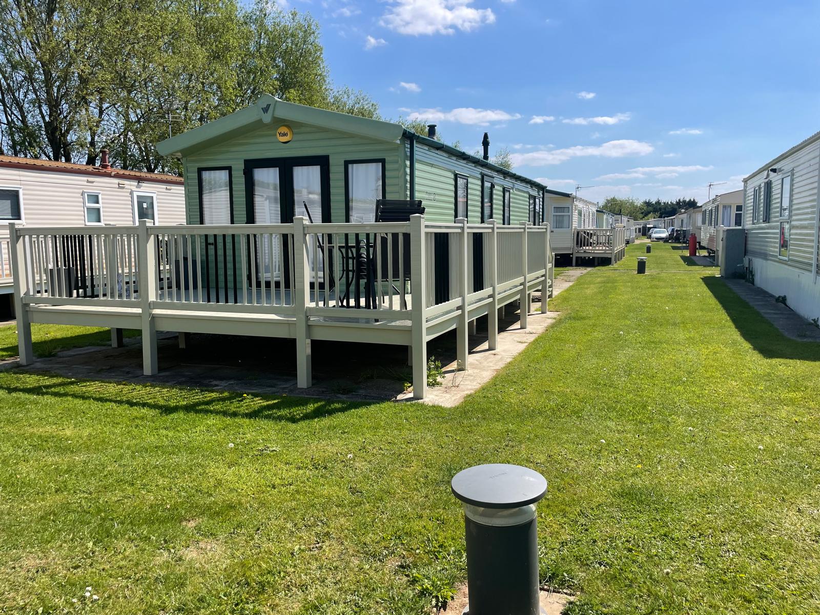 Green holiday trailer with deck on grassy campsite under blue sky