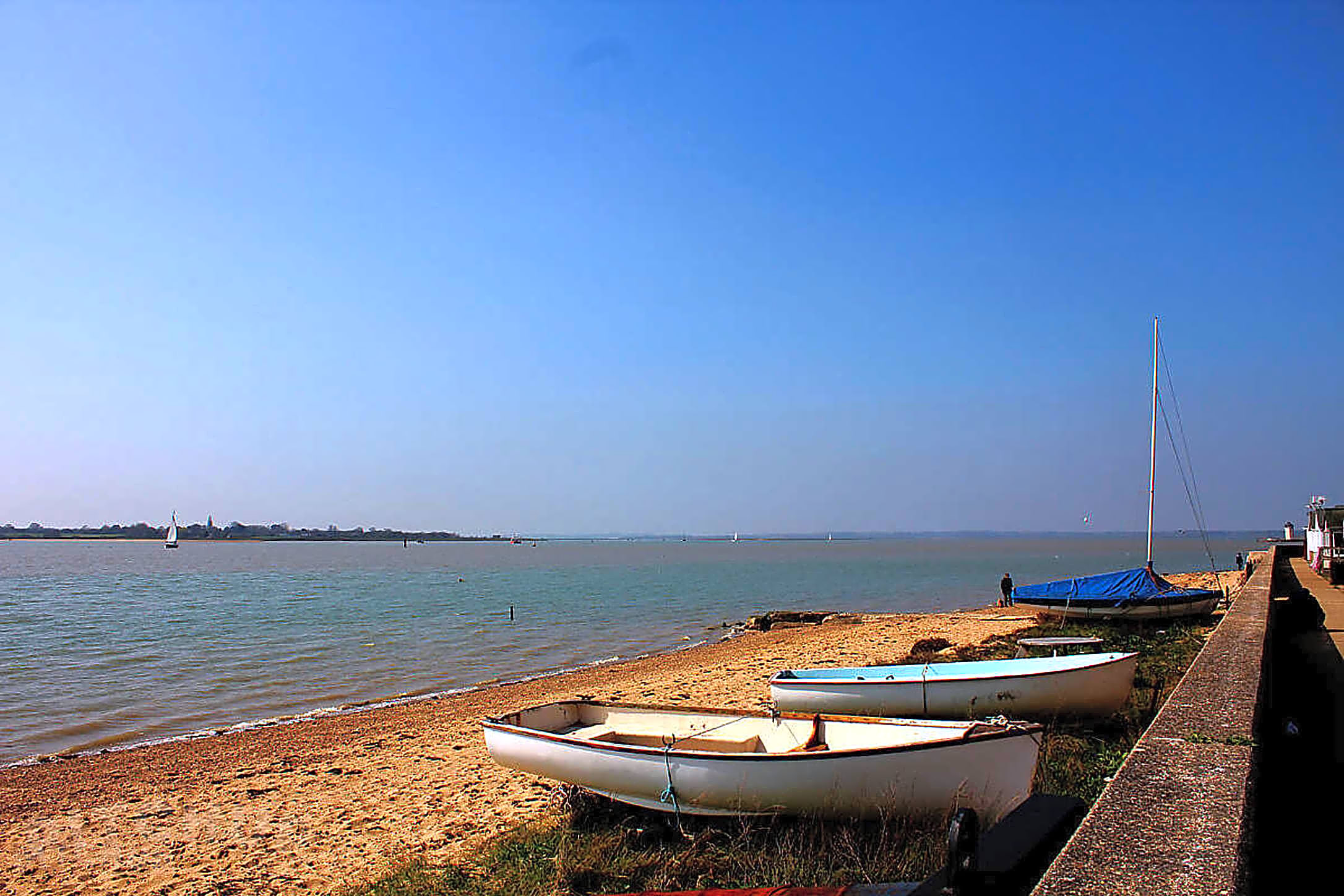 White boats rest on sandy beach with sailboats in calm blue water