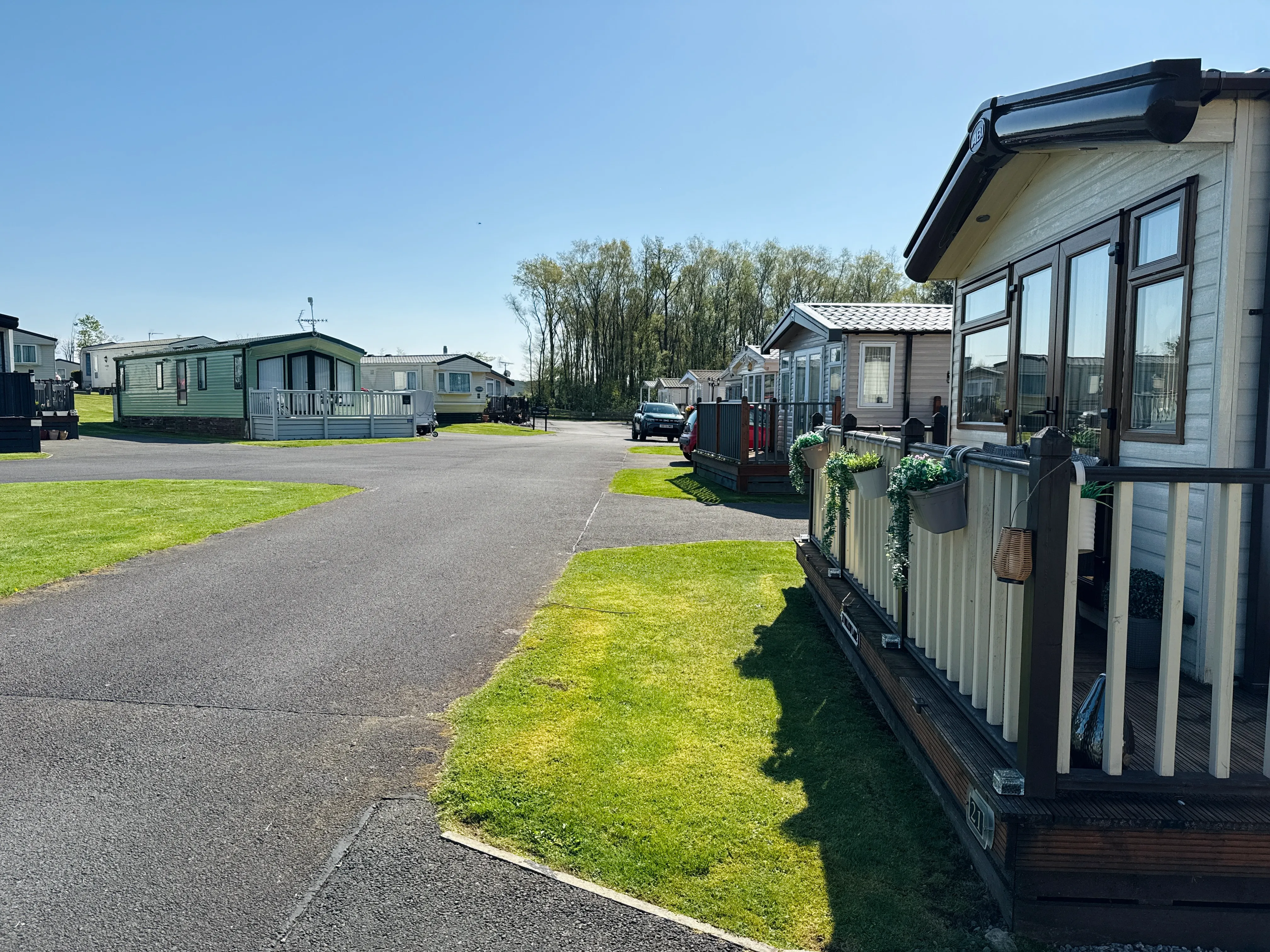 Mobile home park with trailers, paved road, and green lawn on sunny day