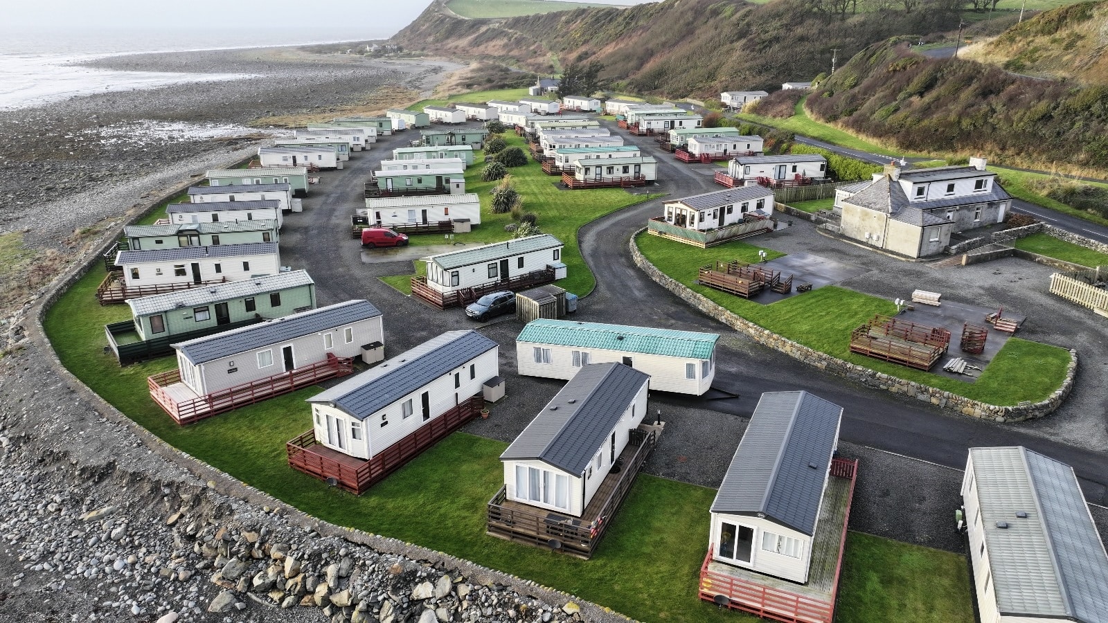 Coastal mobile home park with white trailers nestled on grassy plots near rocky beach