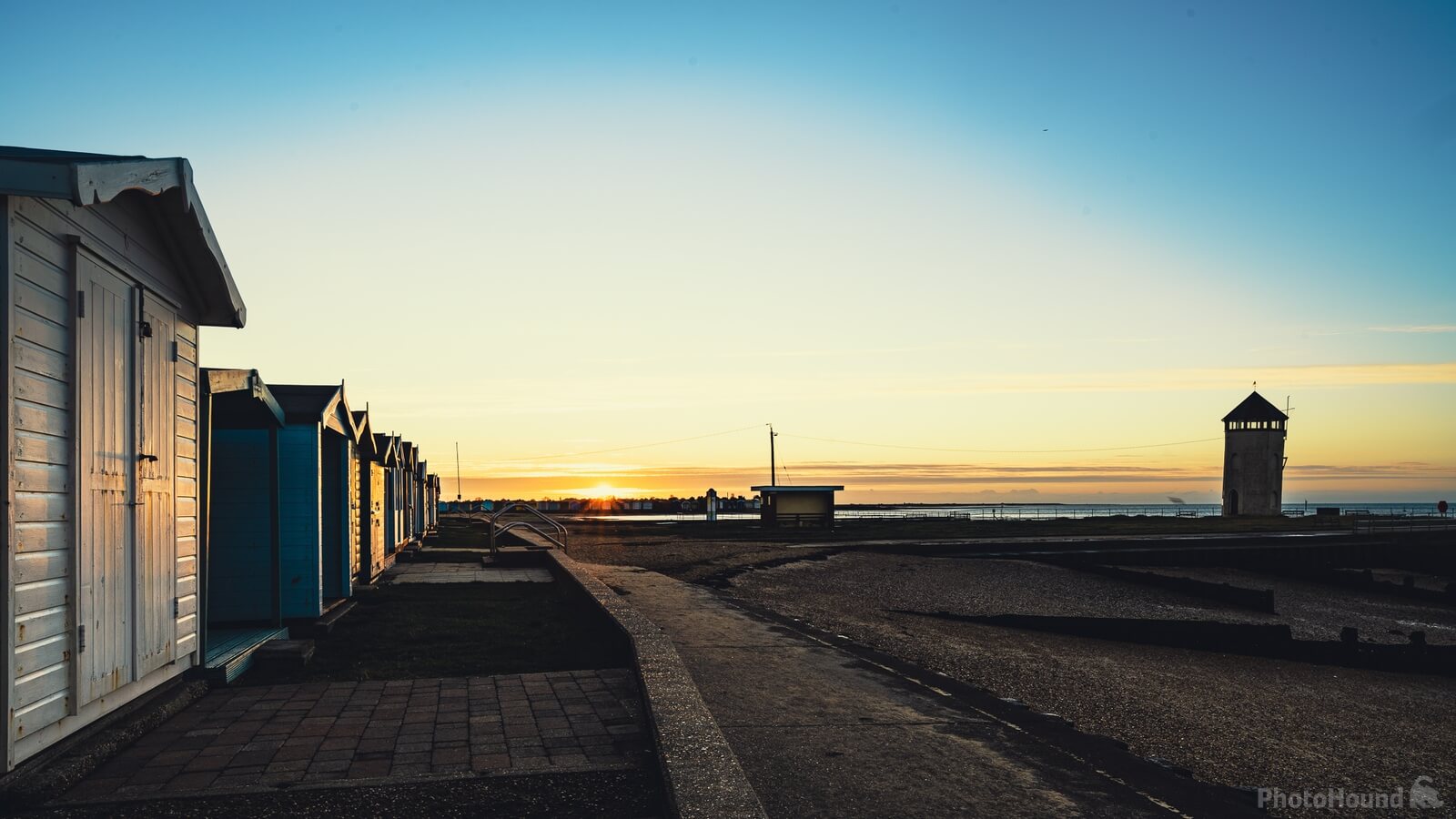 Beach huts at sunrise with watchtower, empty seaside landscape
