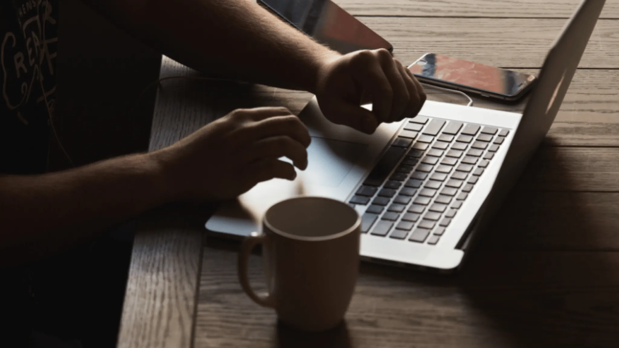 Overhead shot of person typing on a laptop beside a cup of coffee