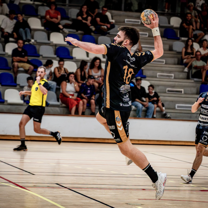 Un joueur du Pouzauges Vendée Handball tire au but pendant un match, sous le regard de l’arbitre et du public. 