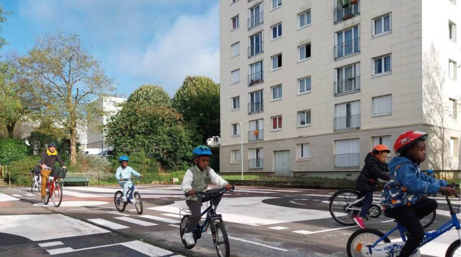 Plusieurs enfants, coiffés de casques, sont à vélo et circulent sur la piste vélo-école au sein du quartier de la Pierre-Heuzé.