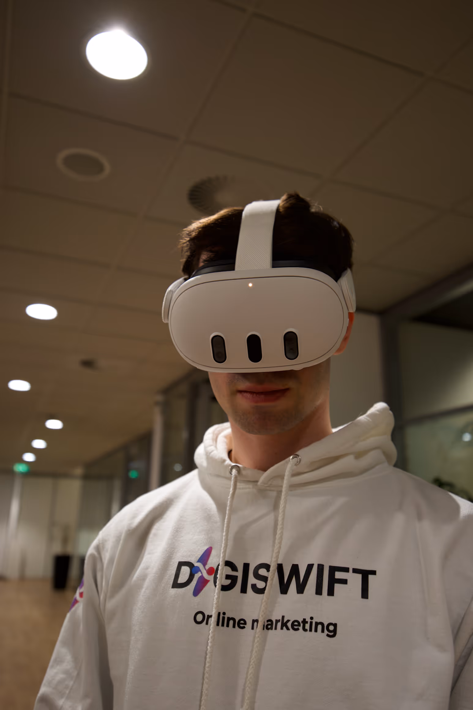 Daniel Coenen, mede-eigenaar en Webflow developer bij DigiSwift, draagt VR-bril en witte DigiSwift hoodie in kantooromgeving met plafondlampen op de achtergrond