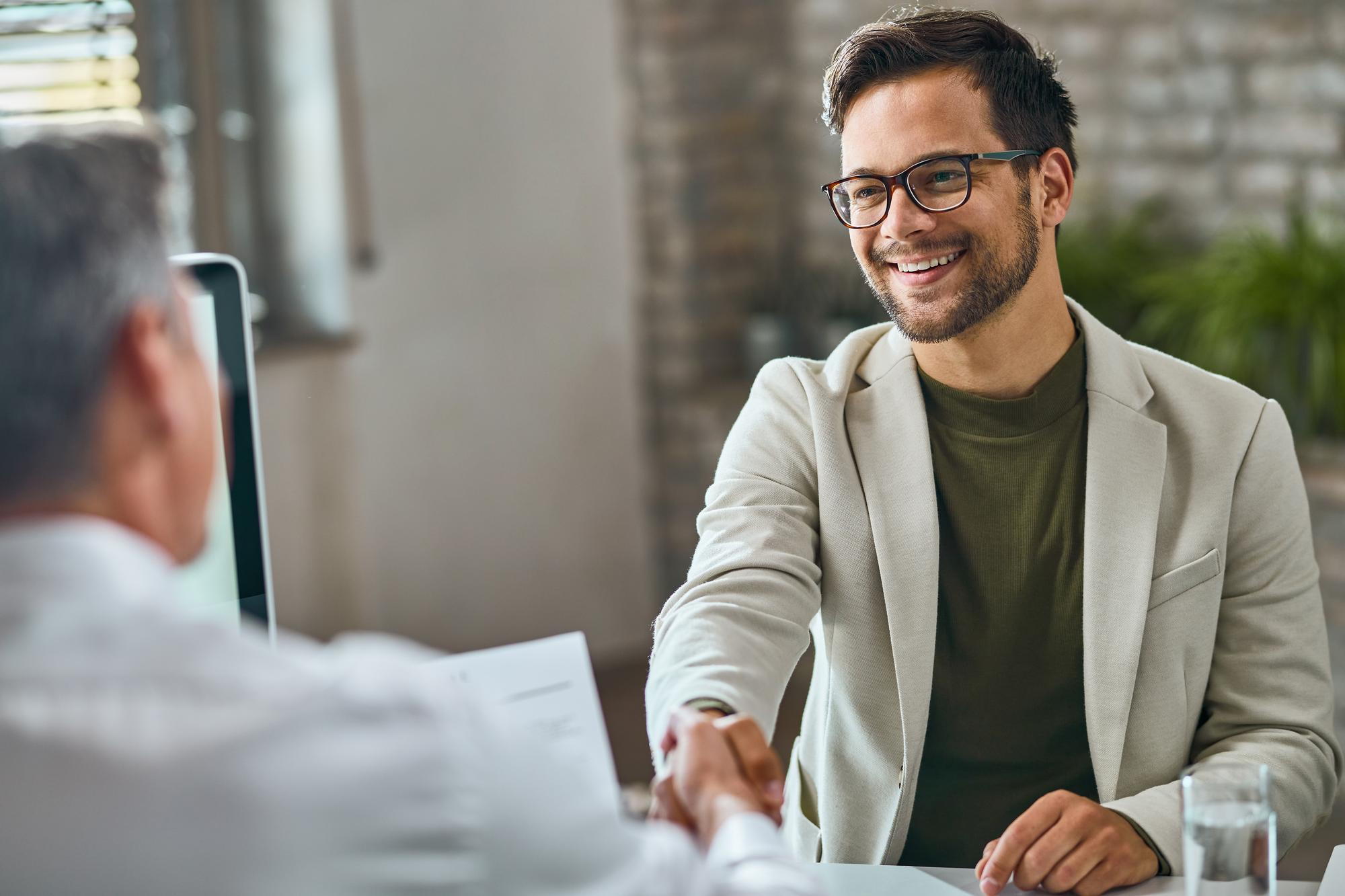 Mannelijke sollicitant glimlacht en schudt handen met recruiter tijdens een sollicitatiegesprek.