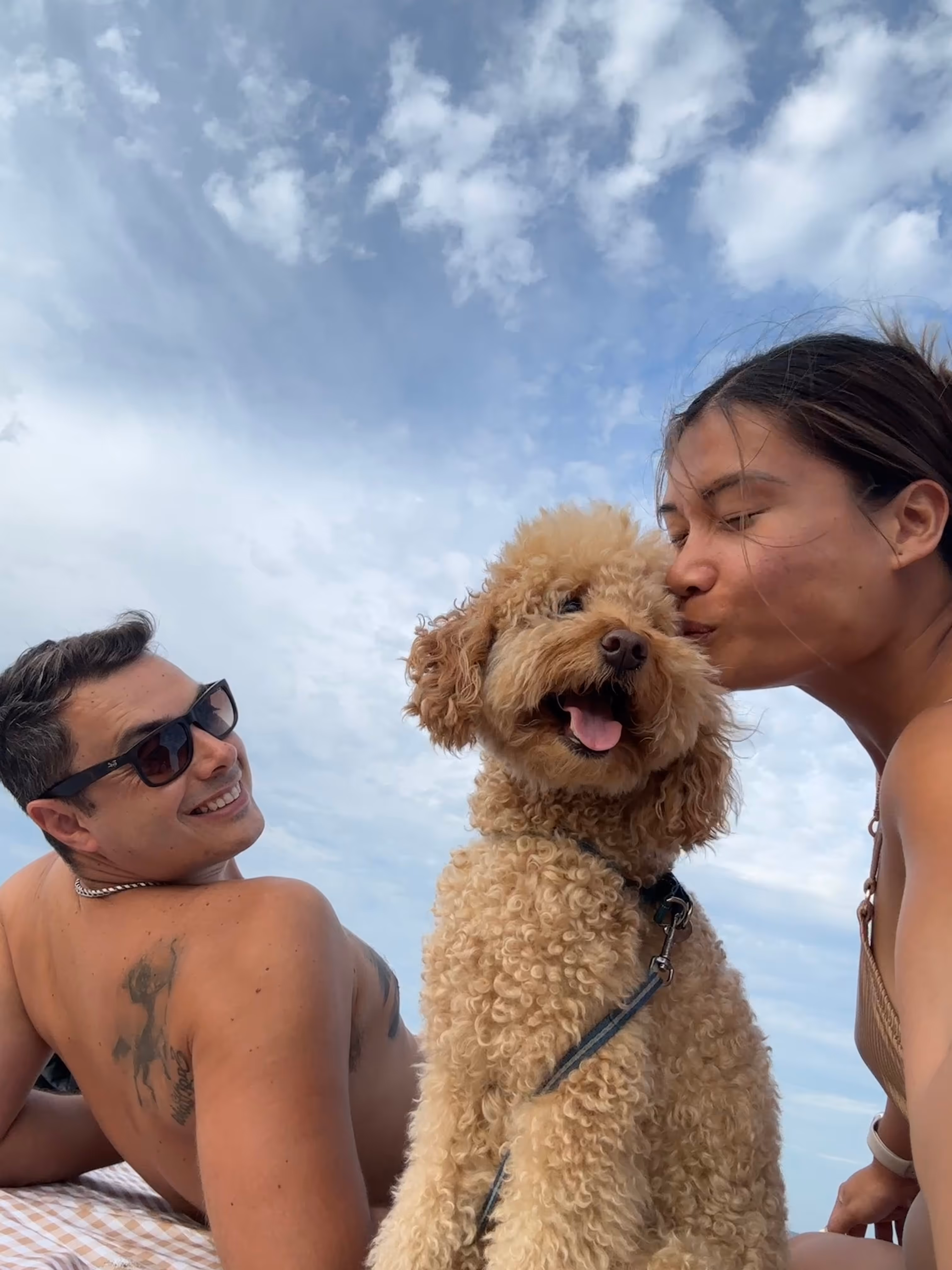 A man and a woman sitting on a beach with a dog.