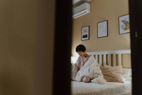 A woman sitting alone on the bed in her bedroom feeling lonely