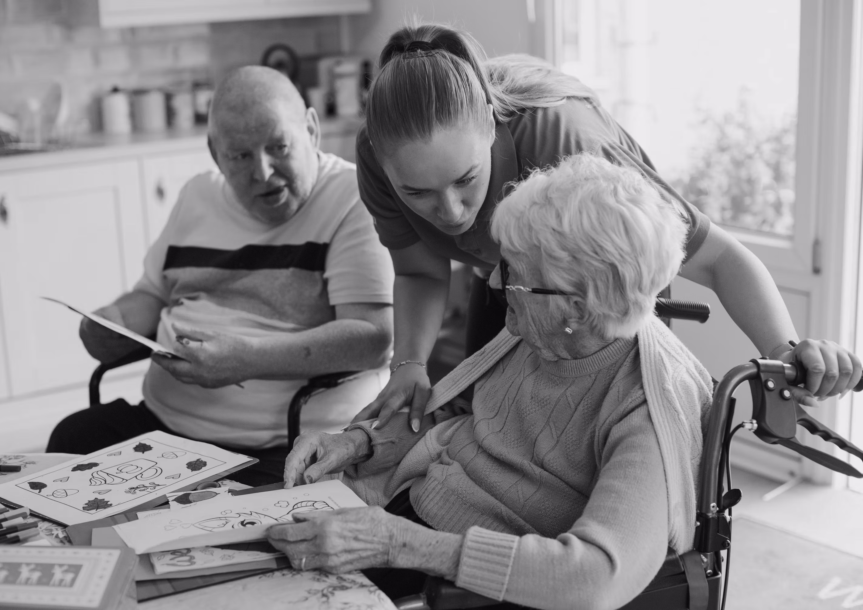 Caregiver assisting two older adults with an activity in a skilled nursing facility.