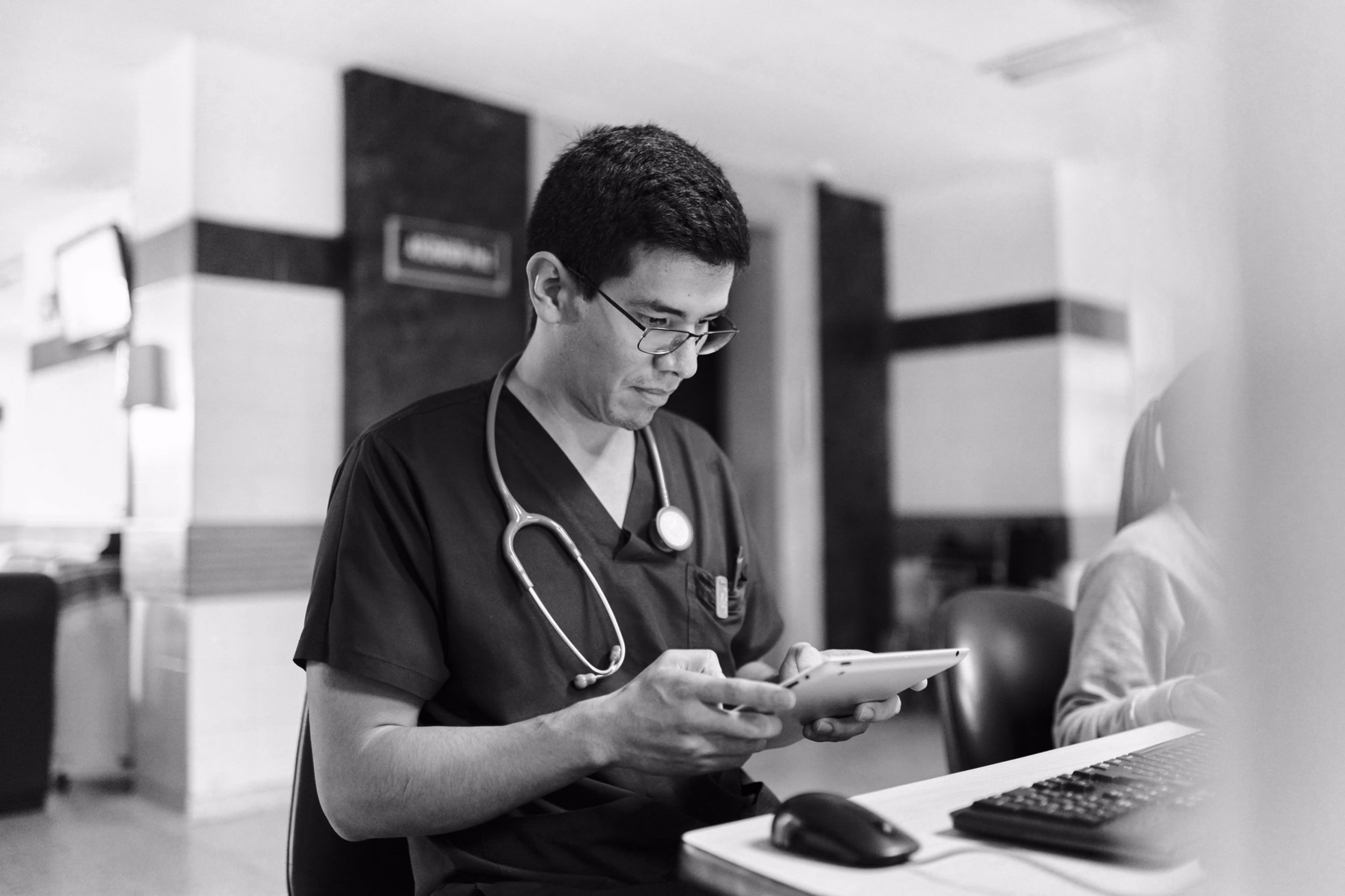 Healthcare professional reviewing patient information on a tablet at a clinical workstation.