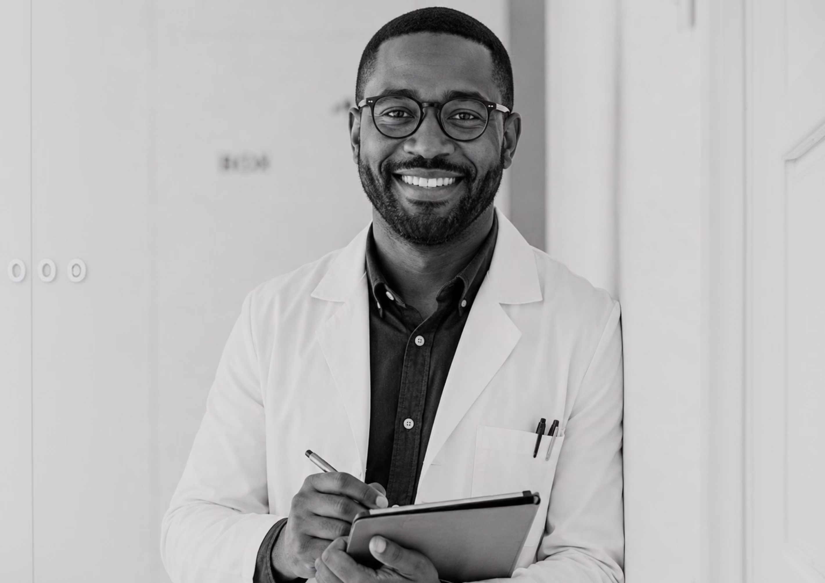 Smiling physician holding a tablet in a clinical setting.