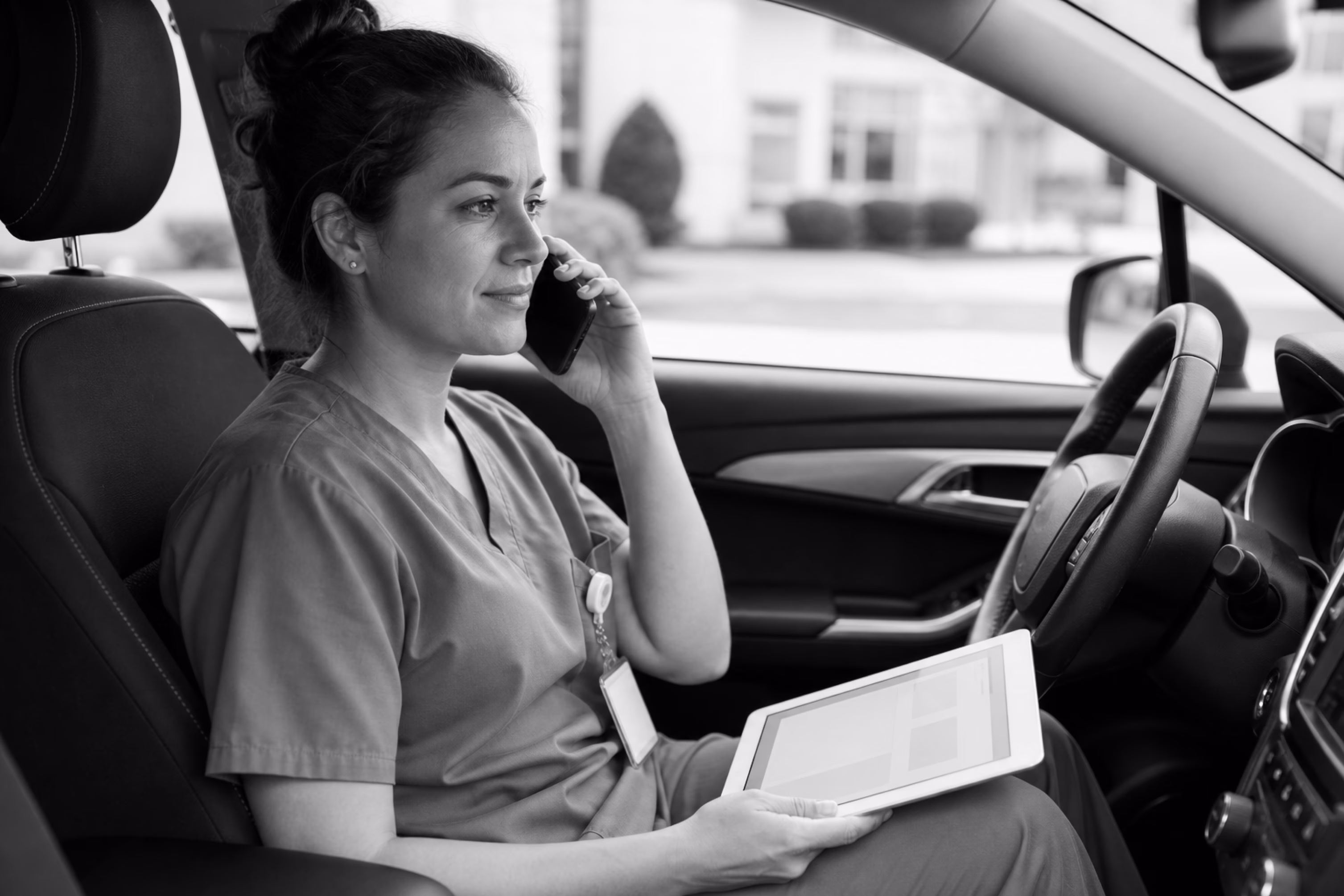 Healthcare professional making a phone call from her car while holding a tablet.