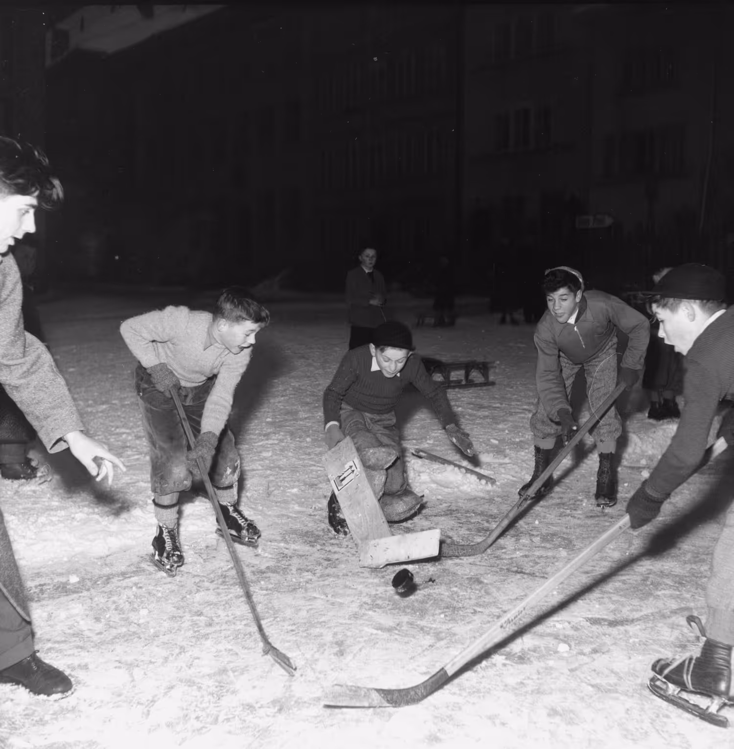Schwarz-Weiß-Foto von Kindern, die nachts auf einer verschneiten Freiluft-Eisbahn Eishockey spielen