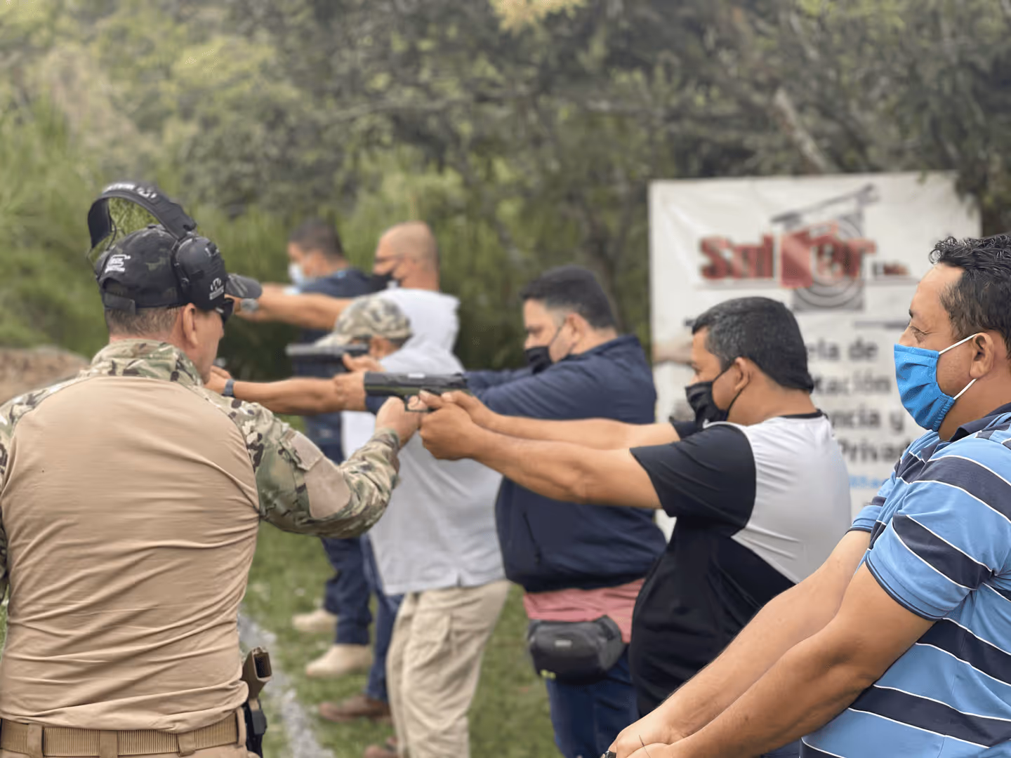 Instructor dando clase de tiro a personas en poligono de campo abierto