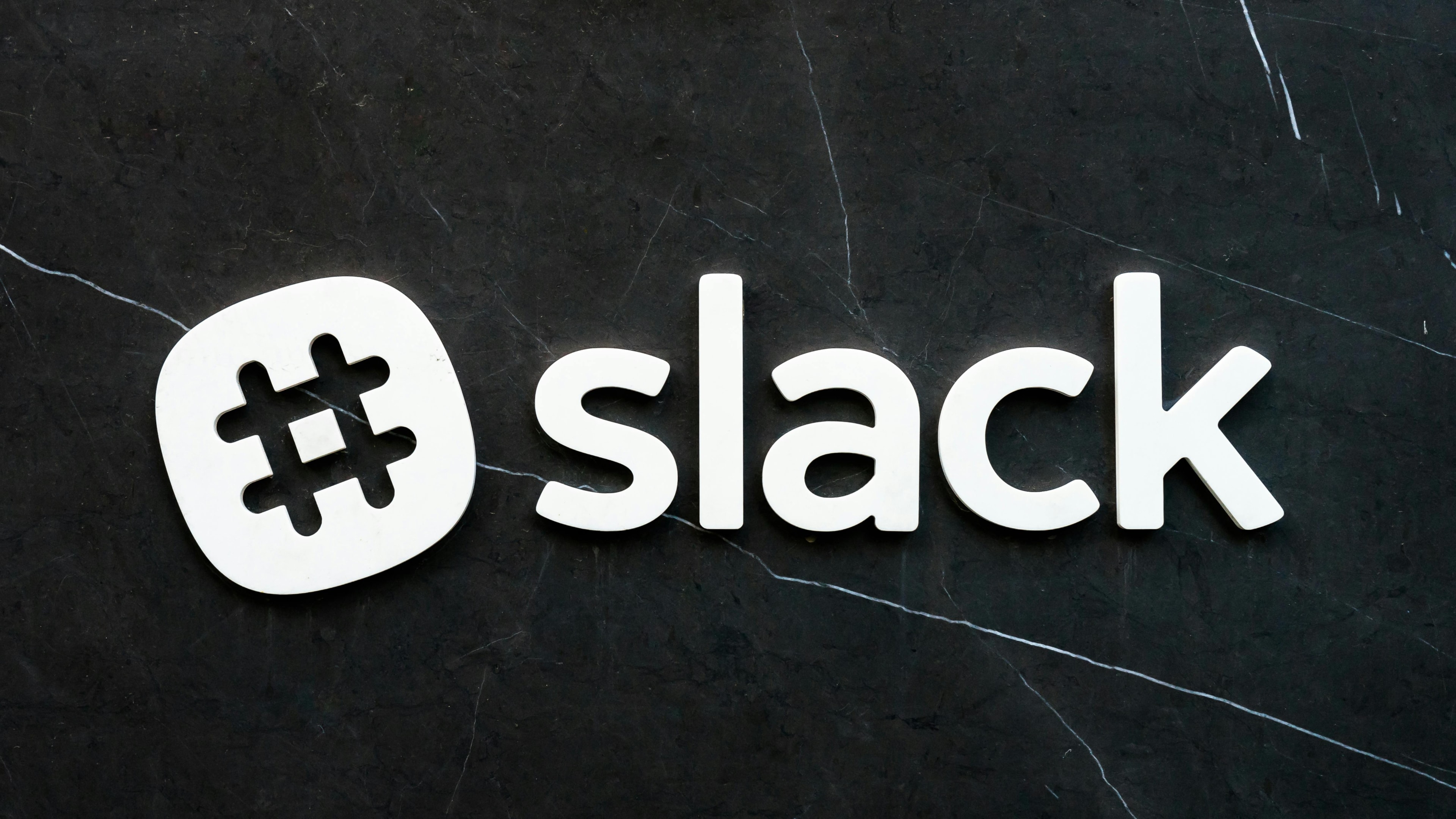 White Slack logo with hashtag symbol on a dark marble background.