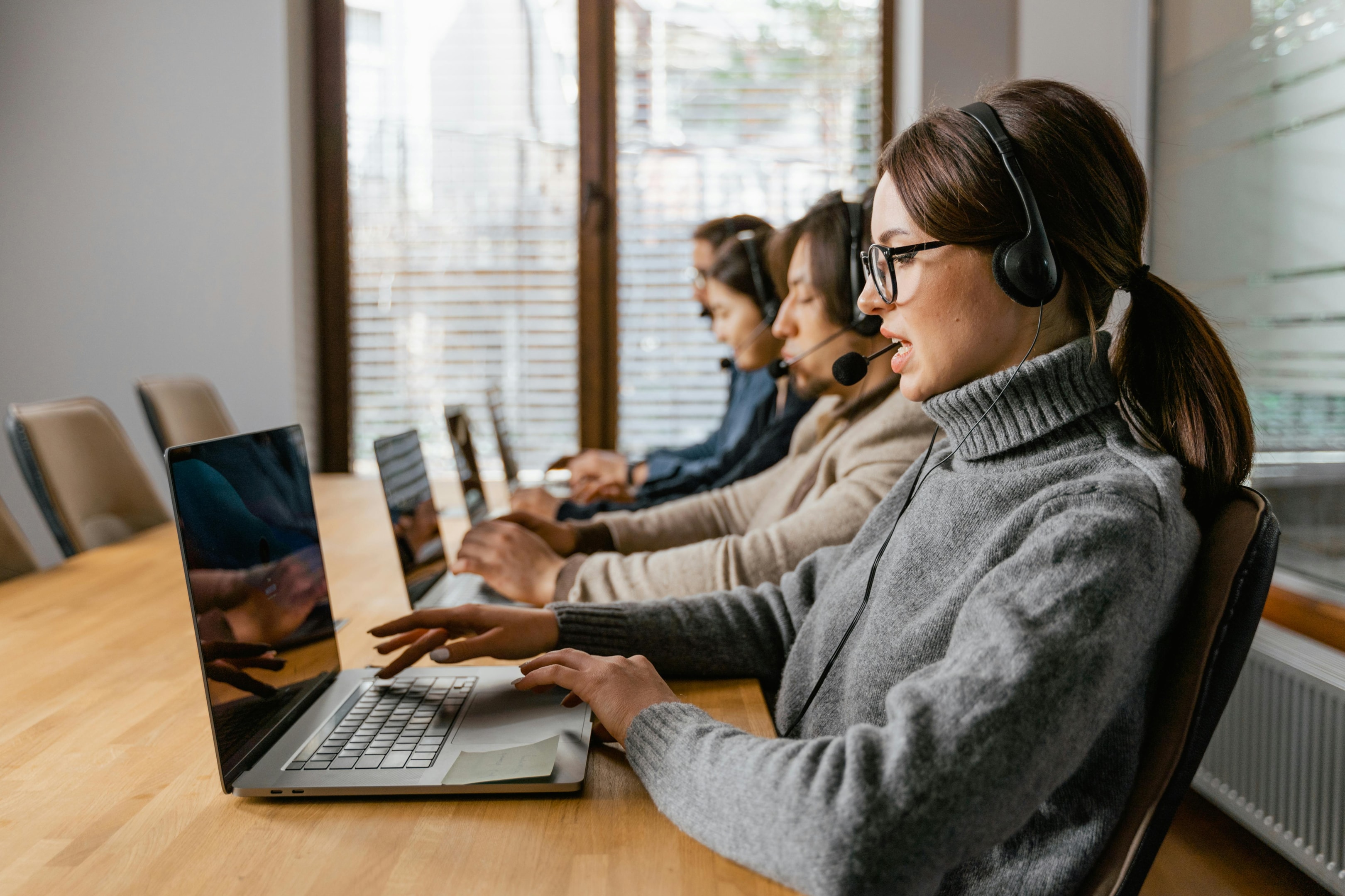 Four people sat at a desk, all working on laptops with head-sets on.