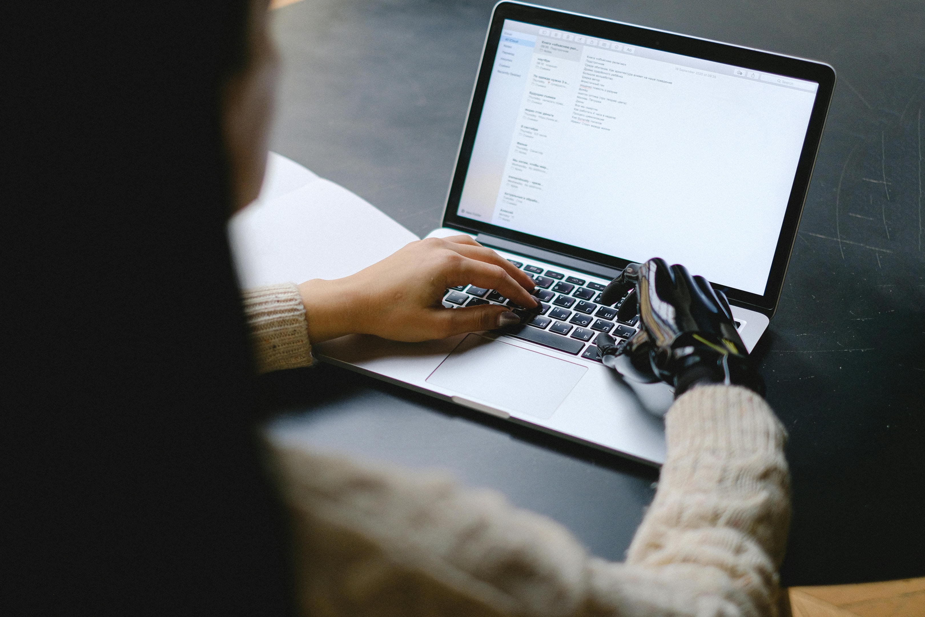 A Person typing on a laptop with a robotic hand, symbolizing AI and human-technology collaboration.