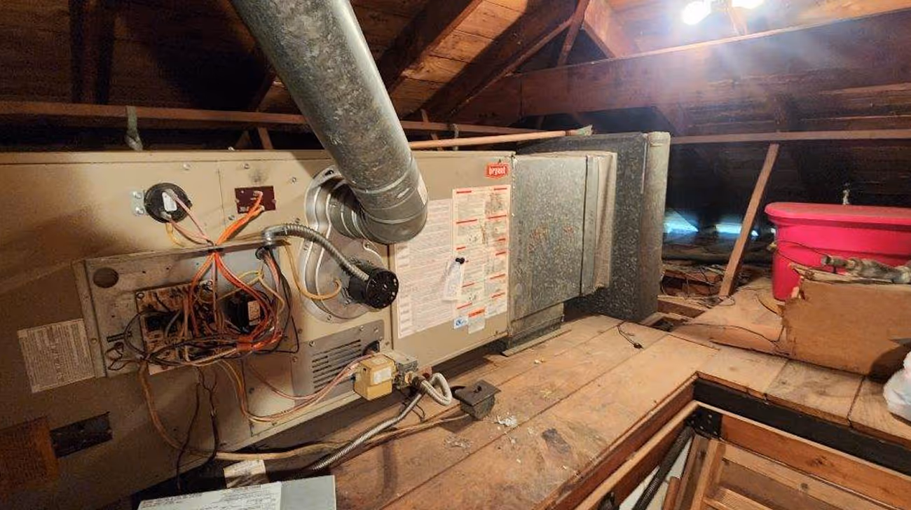 Old HVAC system with exposed wiring in dusty wooden attic space