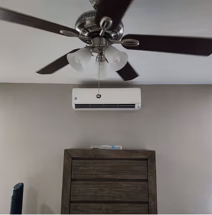 Ceiling fan and wall-mounted air conditioner above wooden dresser