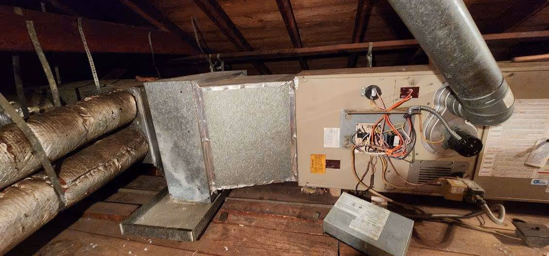 Old HVAC system with exposed wiring in dusty wooden attic space