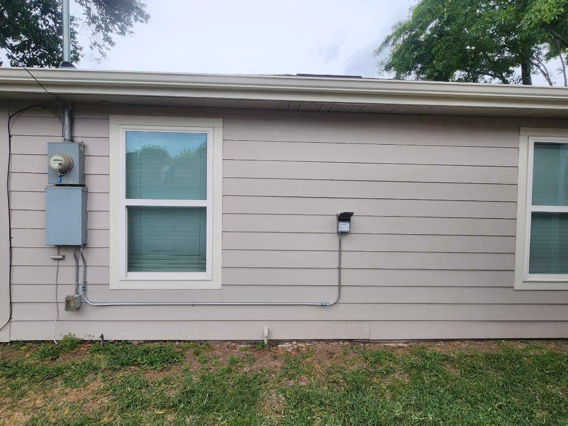 House exterior with electrical meter, windows, and utility boxes on siding