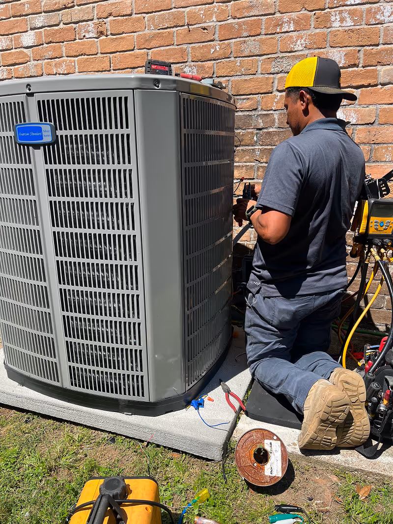 HVAC technician repairing air conditioning unit beside brick wall