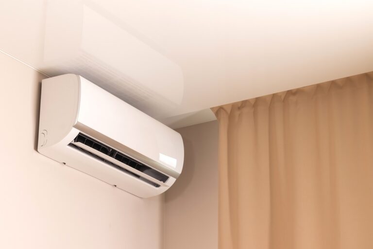  A modern, wall-mounted ductless mini-split air conditioner is installed in the corner of a room, next to a brown curtain.