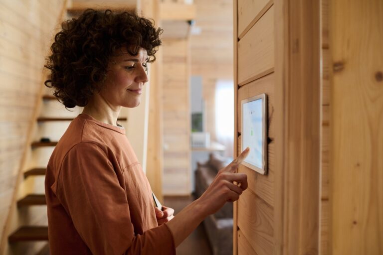  A woman with curly brown hair smiles as she uses a smart home thermostat control panel mounted on a wooden wall.