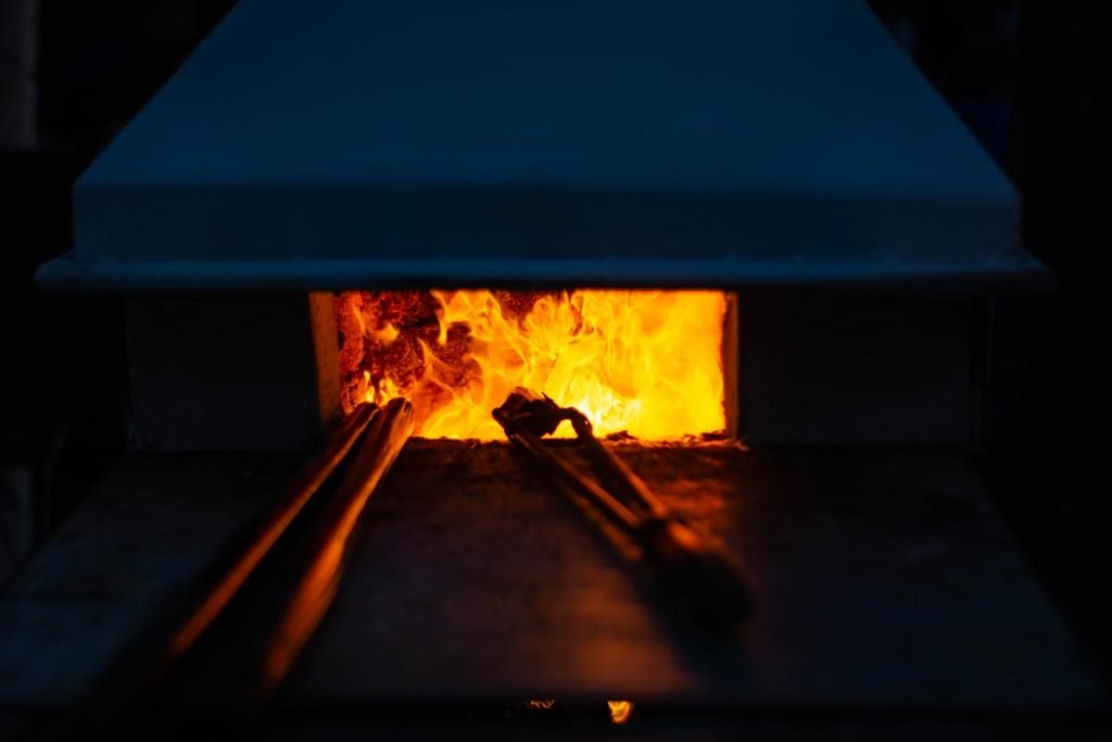 A blacksmith's forge or furnace is glowing with bright orange and red flames, with metal tongs resting on a metal surface in front of the opening.
