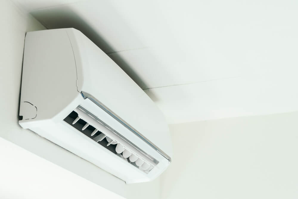  A clean, white, wall-mounted ductless mini-split air conditioner is angled upwards, with its louvers open.