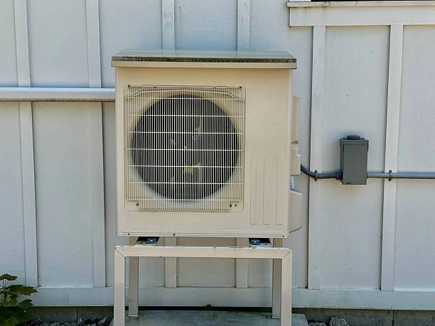 A single outdoor mini-split air conditioner unit is mounted on a stand against a white slatted wall.