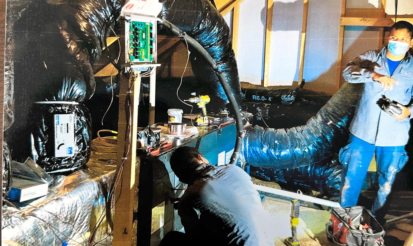 Technicians working on HVAC system with insulated ducts and electronic equipment