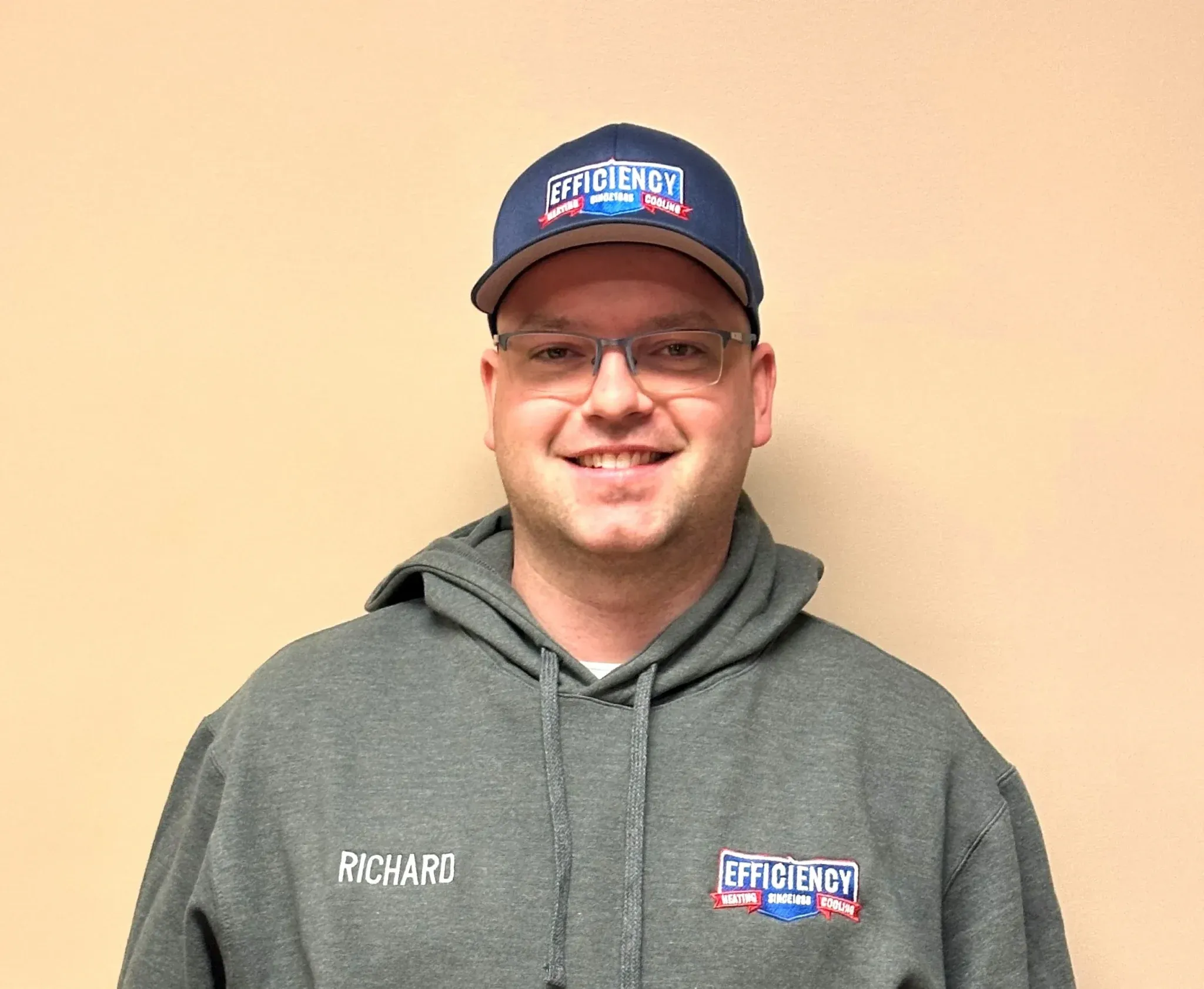 Smiling employee in gray hoodie and Efficiency branded baseball cap