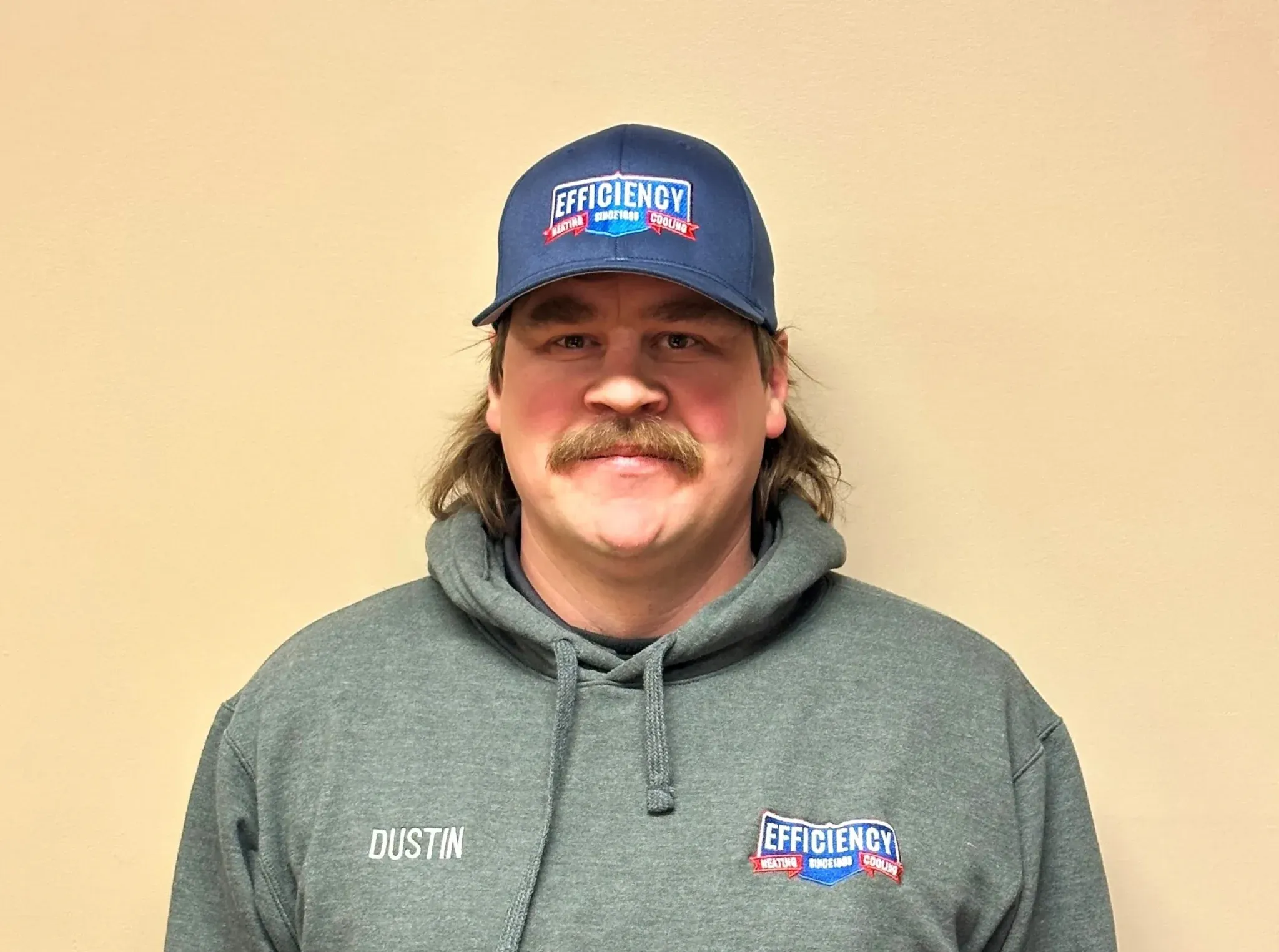 Employee with Efficiency logo hat and hoodie, standing against beige wall