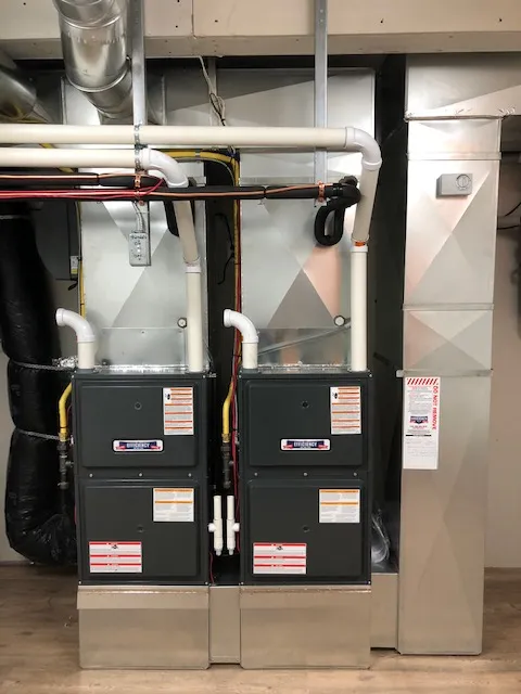 Two black furnaces with white pipes in a utility room
