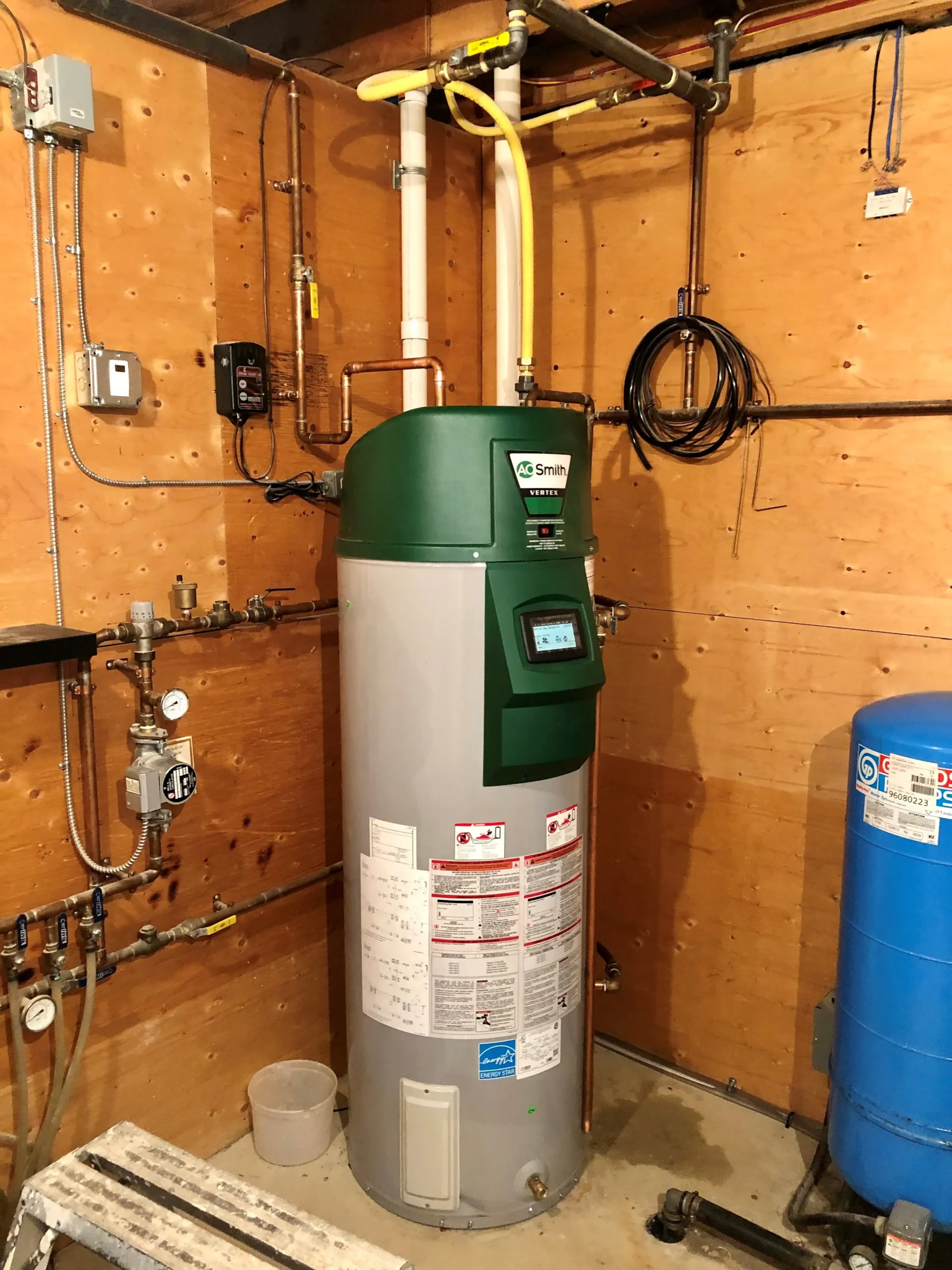 Green and white water heater in utility room with pipes and valves