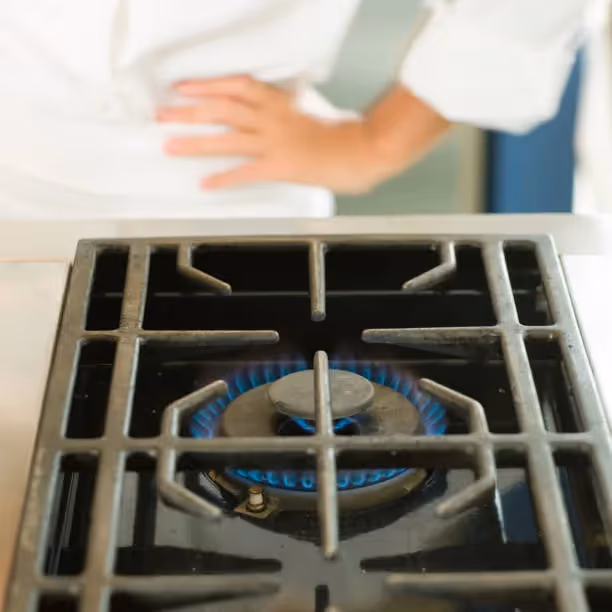 Gas stove burner with blue flame, hand nearby adjusting kitchen appliance
