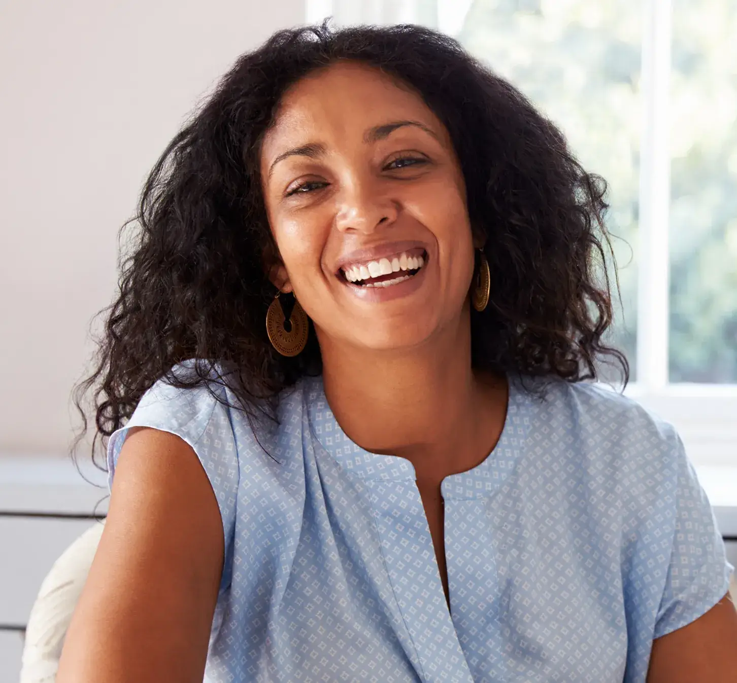 Smiling woman sitting in a bright, comfortable setting.