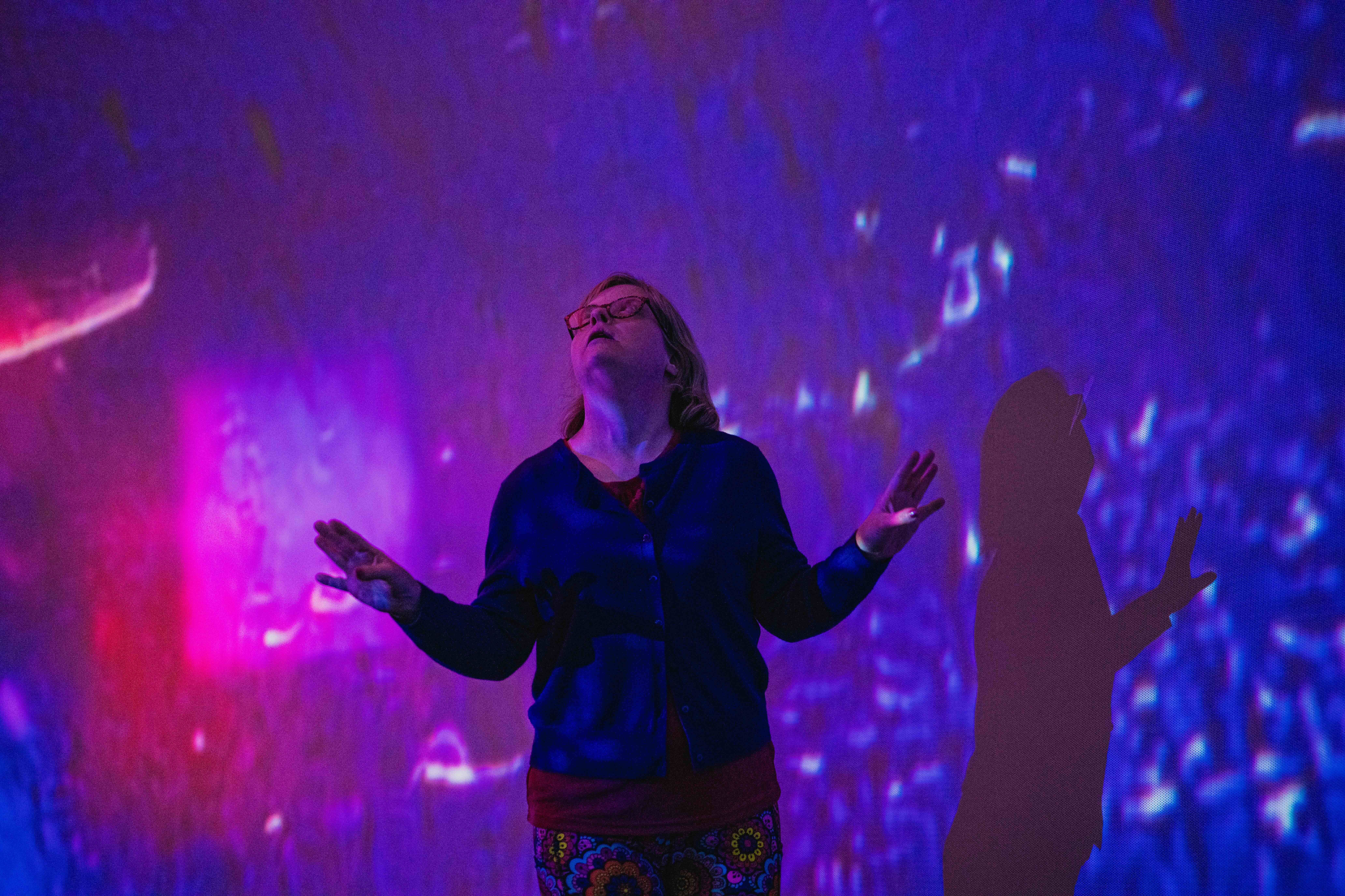 a photo of a woman standing in a purple light projection with her arms raise outwards