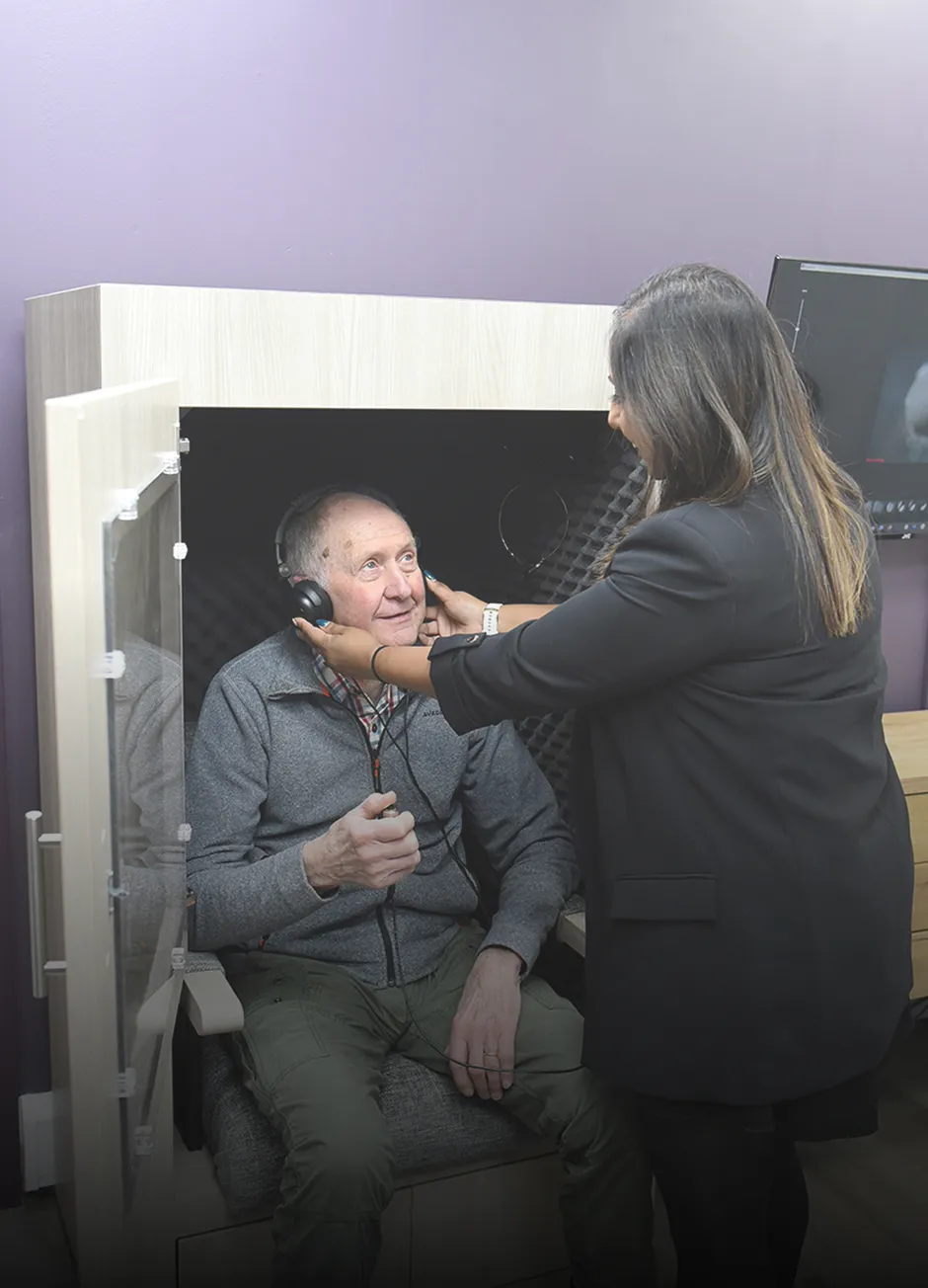 Audiologist fitting headphones on a patient in a hearing test booth