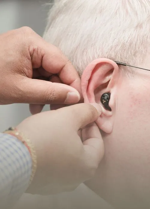 Audiologist fitting a discreet hearing aid into a patient's ear during a private hearing care appointment