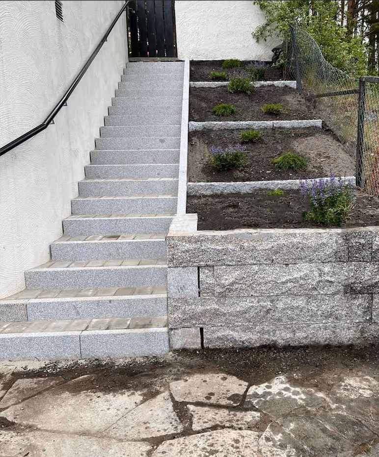 Ferdig trapp i kantstein, med delikat blomsterbed ved siden av. 