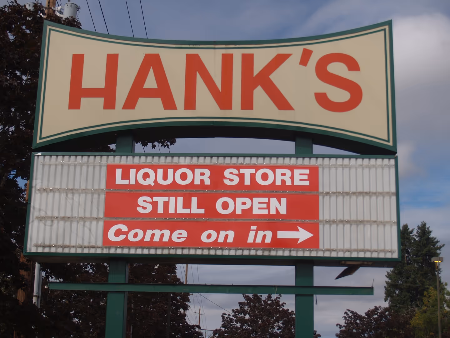 A sign that says hank's liquor store still open come on in.